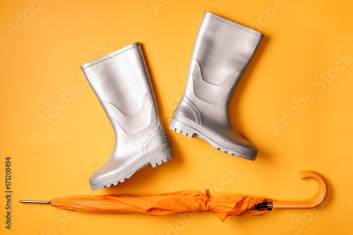 From above shot of stylish silver gumboots and umbrella on orange background.