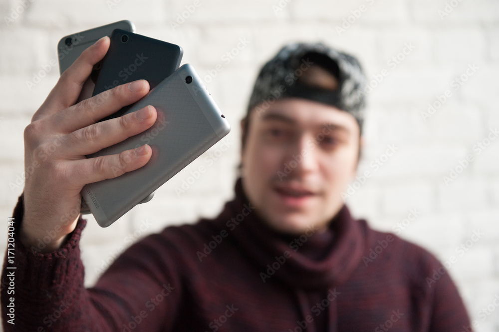Handsome young man looking at three different smartphones in his hand Handsome young man looking at three different smartphones in his hand