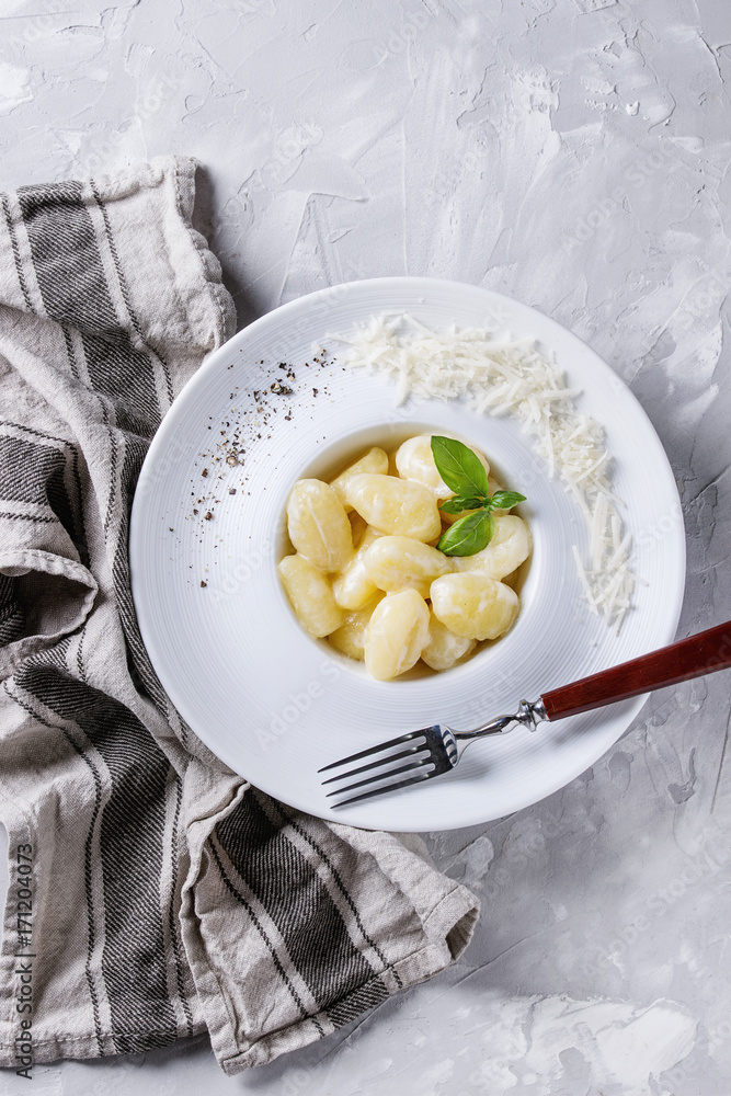 White plate of hot creamy potato gnocchi served with black pepper, grated parmesan, fresh basil, fork on textile napkin over gray concrete background. Flat lay with space White plate of hot creamy potato gnocchi served with black pepper, grated parmesan, fresh basil, fork on textile napkin over gray concrete background. Flat lay with space