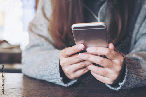 Closeup image of a woman holding ,using and looking at smart phone in modern cafe