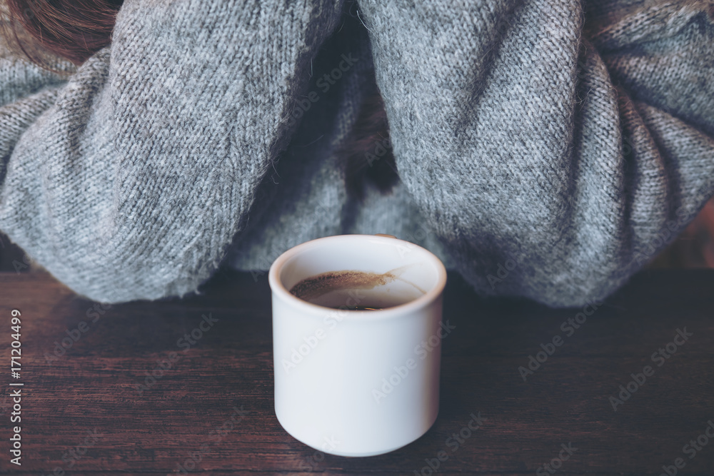 Closeup image of white hot coffee cup on vintage wooden table in cafe with woman in background Closeup image of white hot coffee cup on vintage wooden table in cafe with woman in background