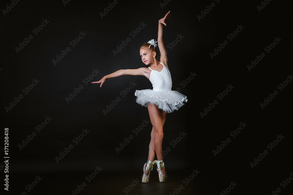A small young ballerina performs an element of ballet dance on a black background.
