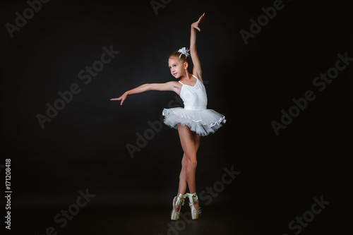 Print op canvas A small young ballerina performs an element of ballet dance on a black background
