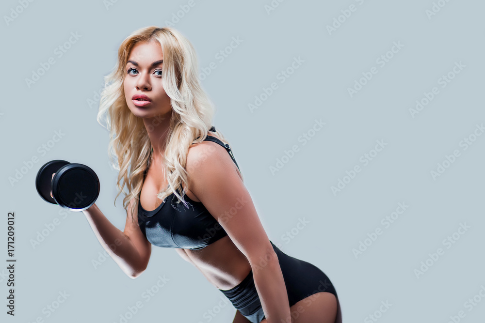 beautiful blonde girl slim figure, with makeup, in a black sports underwear is with dumbbells in hands, looking down, gray background, isolate, fitness, cross, fit, sports, beautiful blonde girl slim figure, with makeup, in a black sports underwear is with dumbbells in hands, looking down, gray background, isolate, fitness, cross, fit, sports,