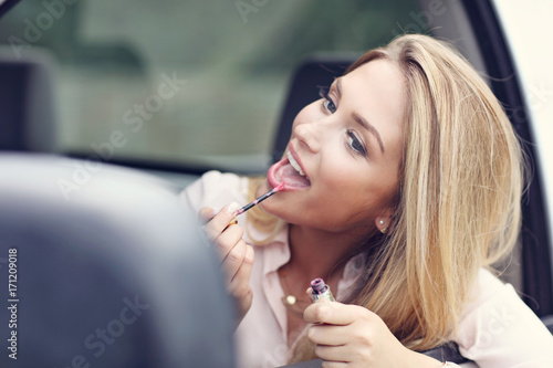 Young attractive woman looking in rear view mirror applying lipstick