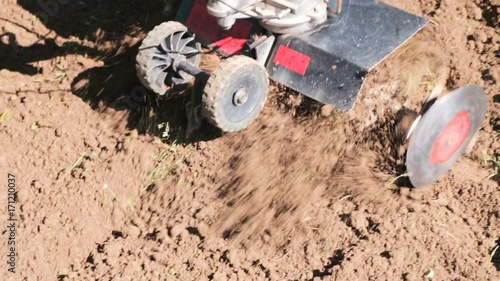 Wallpaper Mural A man is a farmer in a suburban area, a vegetable garden, plows the land with a cultivator, a manual motor plow, throwing clay and soil. Close-up of a cultivator of a tractor Torontodigital.ca