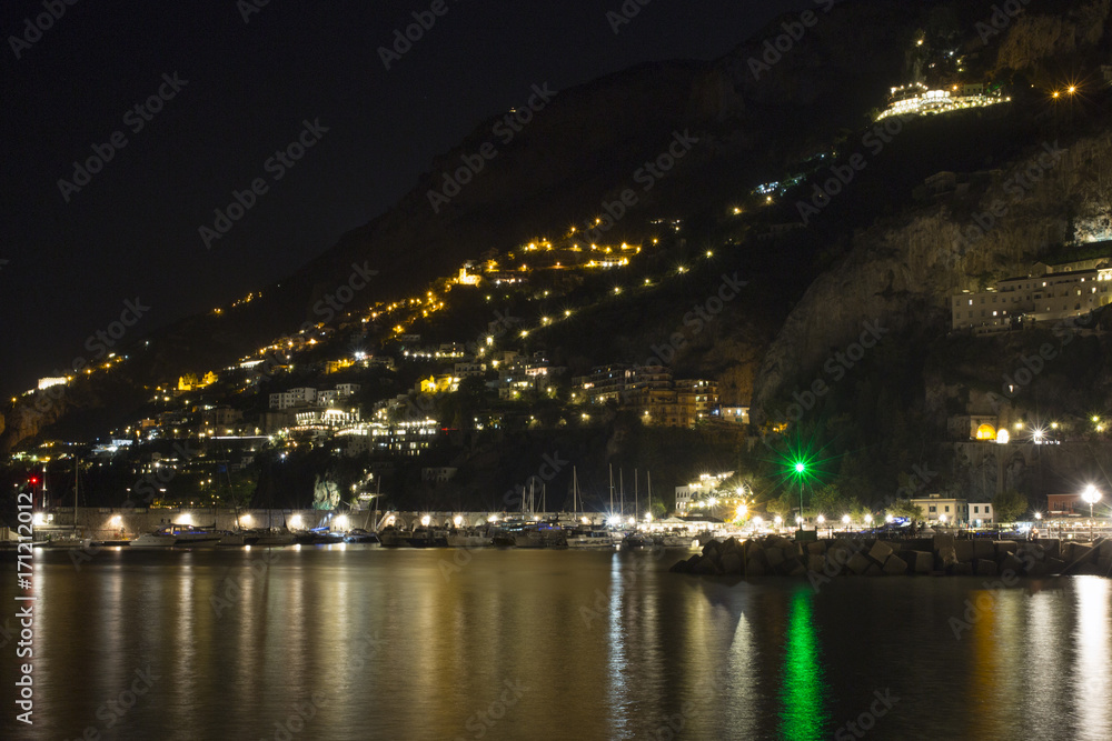 Panorama notturno della citta di amalfi in costiera Amlfitana, Campania, Italia. Nella notte le luci del porto e del lungomare si riflettono sull'acqua del mare scuro.