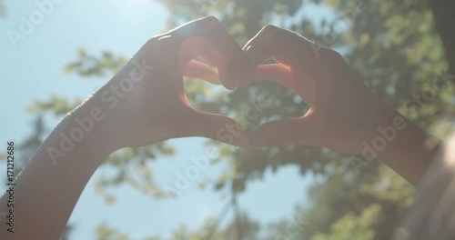 Female hands in shape of heart over green nature and blue sky. 