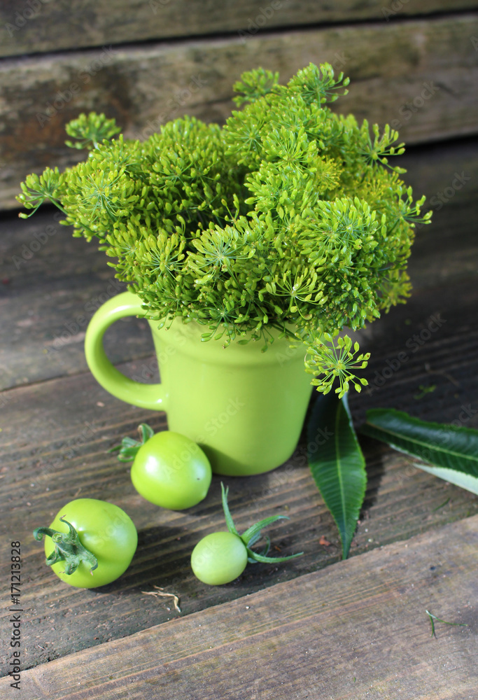 Dill in green coffee mug on wooden background with tomato and leaves Dill in green coffee mug on wooden background with tomato and leaves