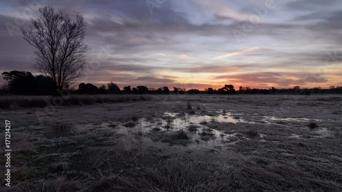 Sunrise over a frozen moor with red clouds reflecting in ice