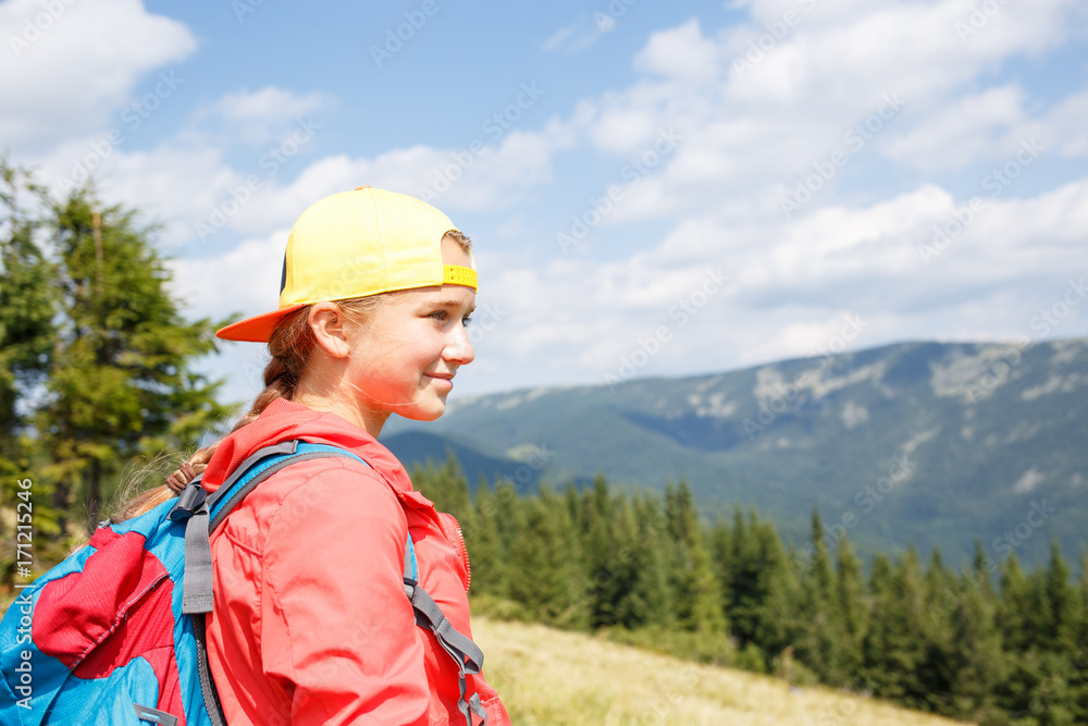 Young smiling teenage girl with backpack enjoying view in mountains. Summer vacation hiking concept background with copy space