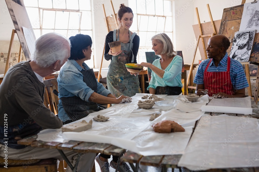 Female instructor showing clay pots to senior people Female instructor showing clay pots to senior people