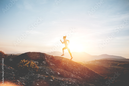 Athletic girl running in the mountains enjoying the sunset. Sport tight clothes. Intentional motion blur.