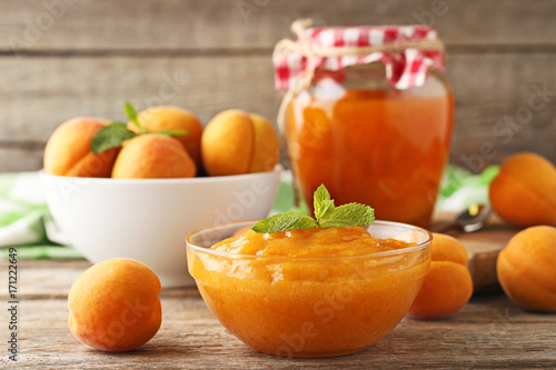 Apricot jam in glass bowl and jar on wooden table