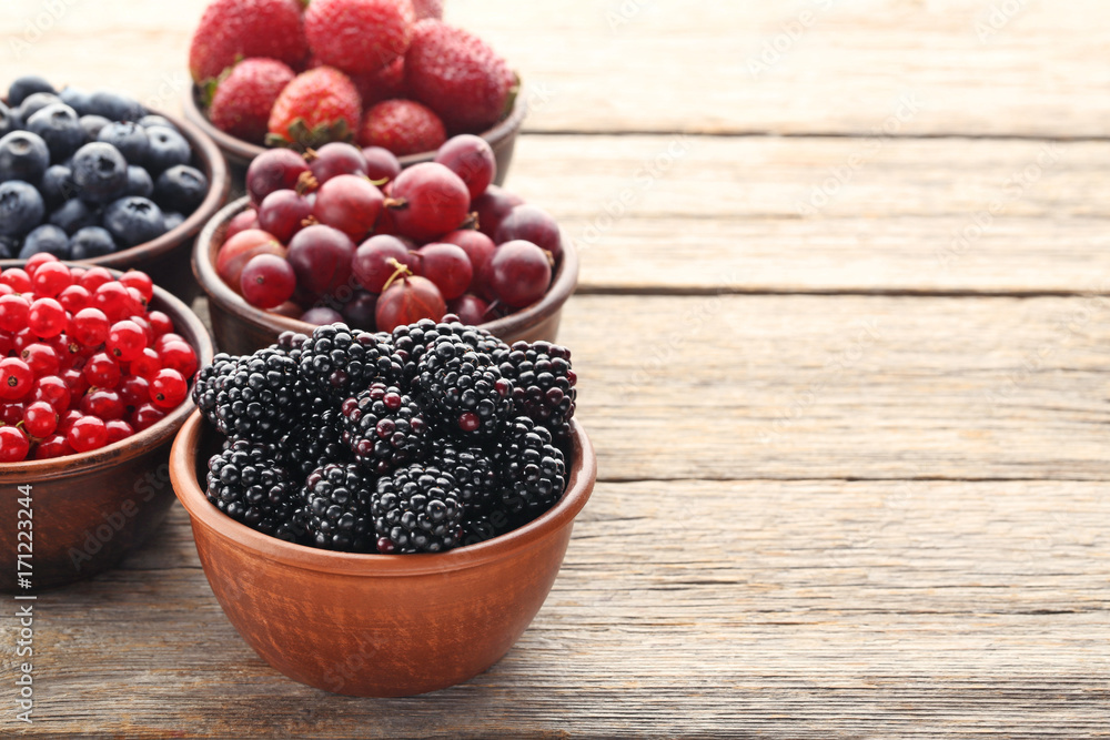 Ripe and sweet berries in bowls on wooden table Ripe and sweet berries in bowls on wooden table