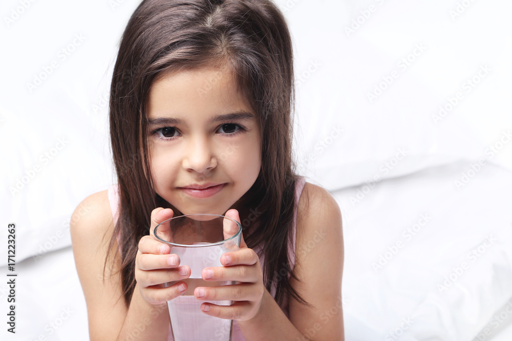 Beautiful little girl drinking water on white bed Beautiful little girl drinking water on white bed