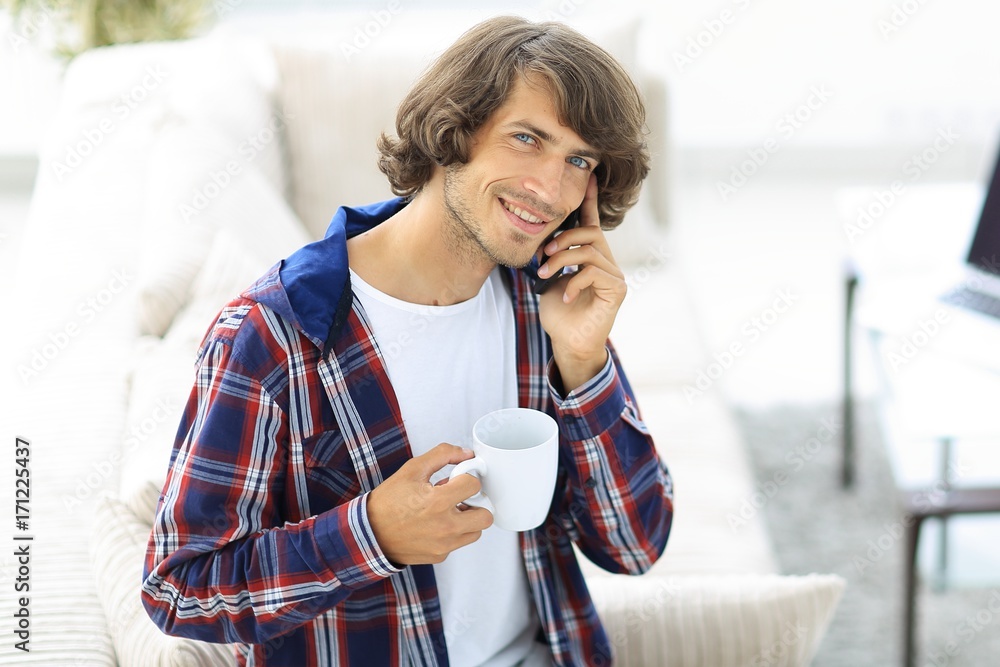 beautiful guy with a cup sits in front of a laptop. beautiful guy with a cup sits in front of a laptop.