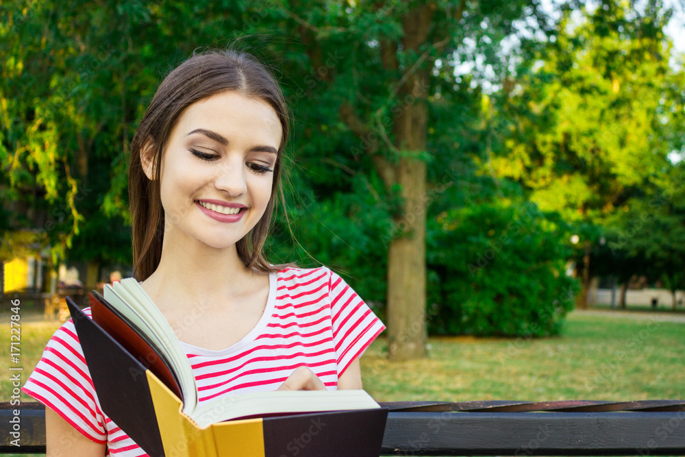 Obraz premium Young smiling woman sitting with diary making some notes in beautiful city park