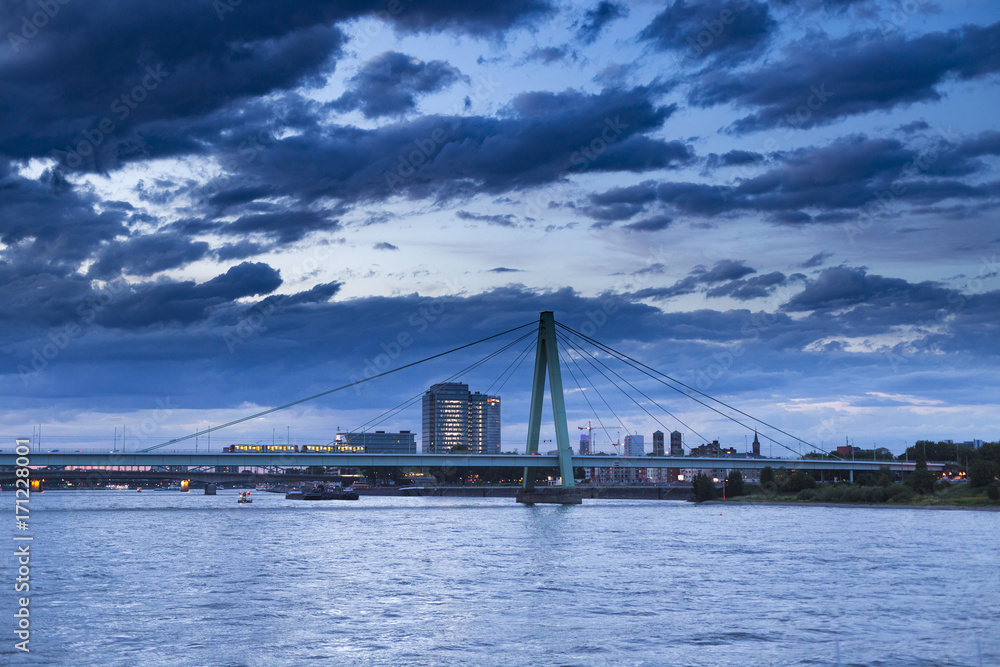 Cityscape with Rhine river,  bridge and cloud sky. Night view at Rhine and Severin Bridge with running tram in Cologne