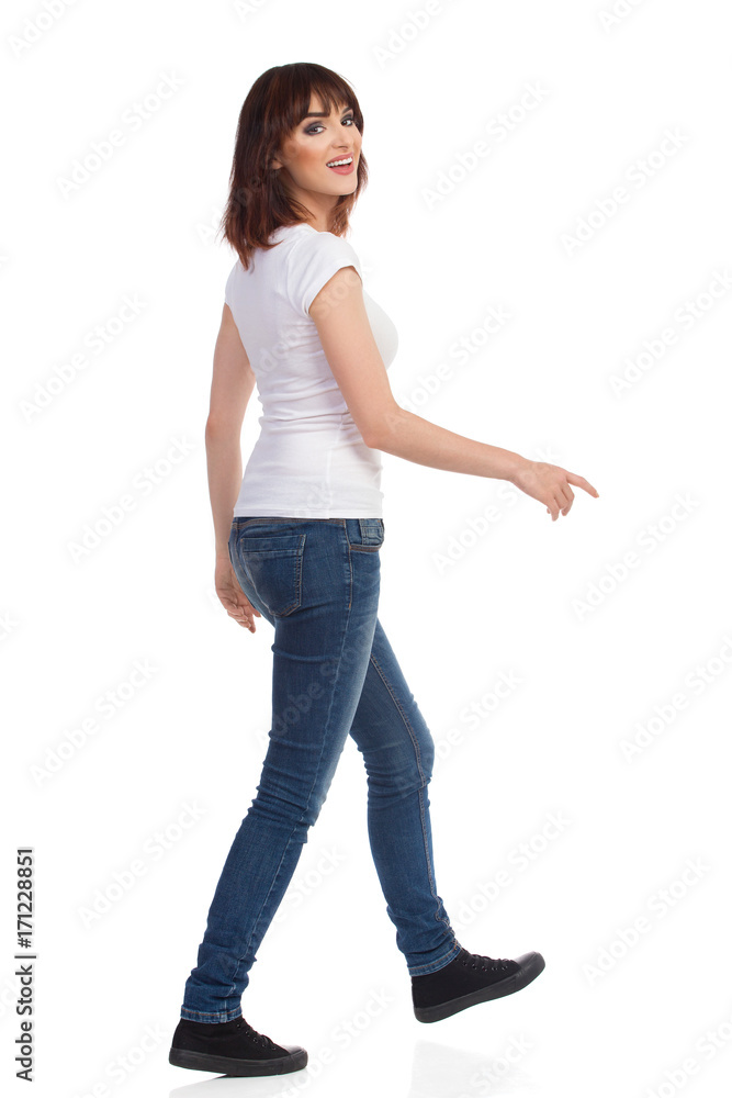 Young Woman Is Walking And Looking At Camera Over The Shoulder Young Woman Is Walking And Looking At Camera Over The Shoulder