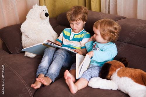 Cute boy and his little sister reading a book together at home 