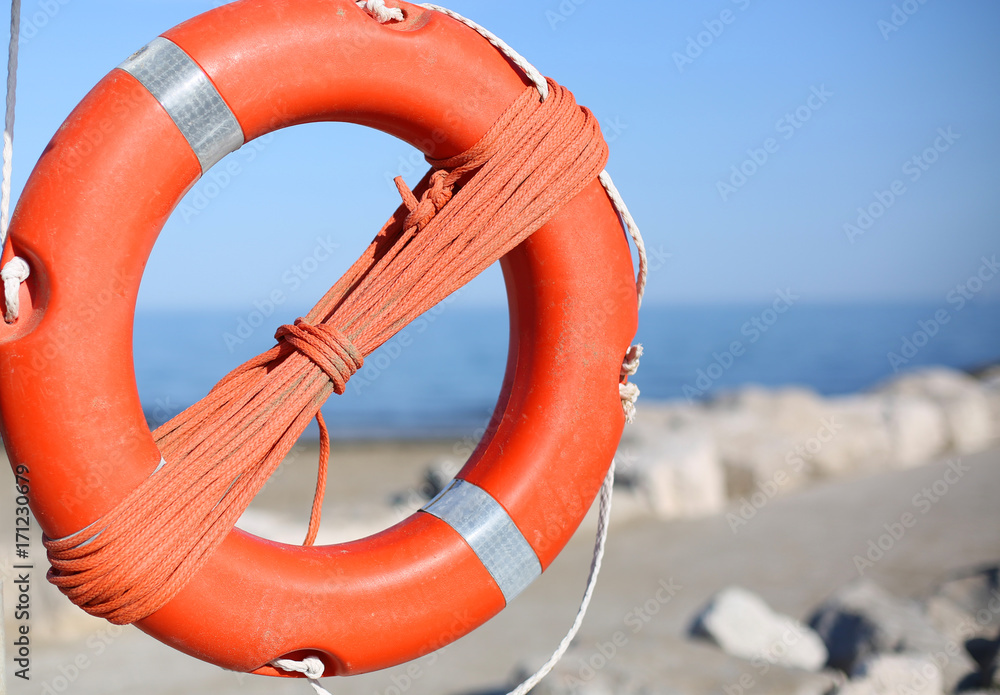 Orange lifebuoy for people near rocks at the sea