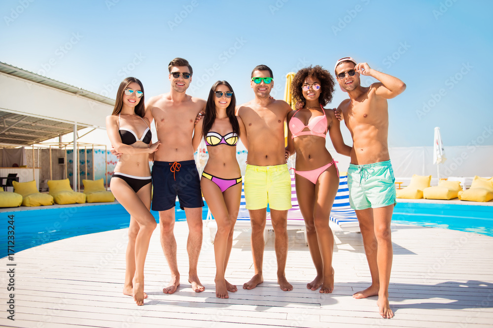 Swim pool sunny party Full length of three cute pairs of lovers, posing in swimming suits and eyewear, holding arms, chinese is with raised up hand, they have fun and enjoy together, great vacation