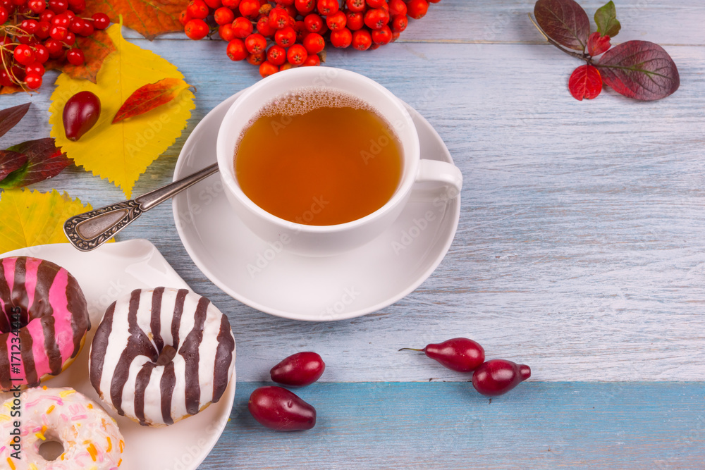 cup of tea and donuts with autumn multicolored leaves and berries on a rustic wooden background, copy space cup of tea and donuts with autumn multicolored leaves and berries on a rustic wooden background, copy space