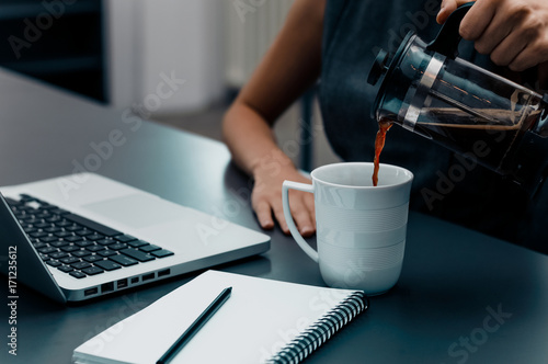 Woman hands pouring coffee into cup on office table.