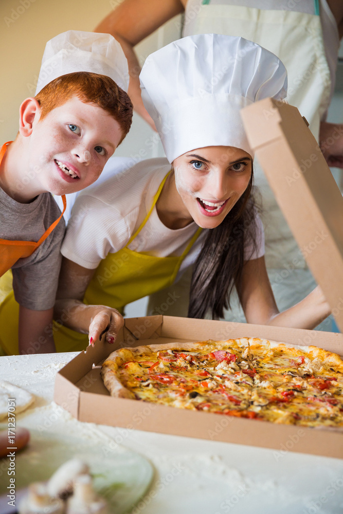 Portrait of young cook woman and her son who standing in the kitchen and sniffing pizza Portrait of young cook woman and her son who standing in the kitchen and sniffing pizza