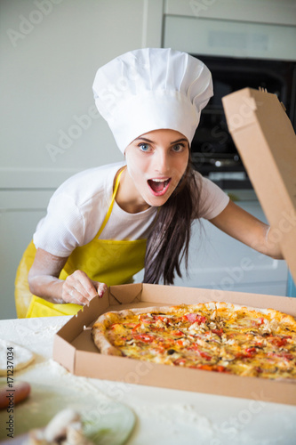 Portrait of young cook woman who standing in the kitchen and sniffing pizza