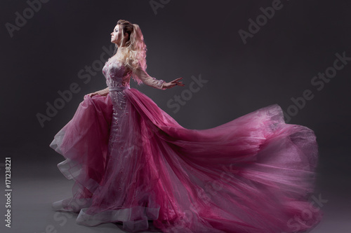 Glamorous lady in a chic pink dress with a train. Studio portrait on gray background