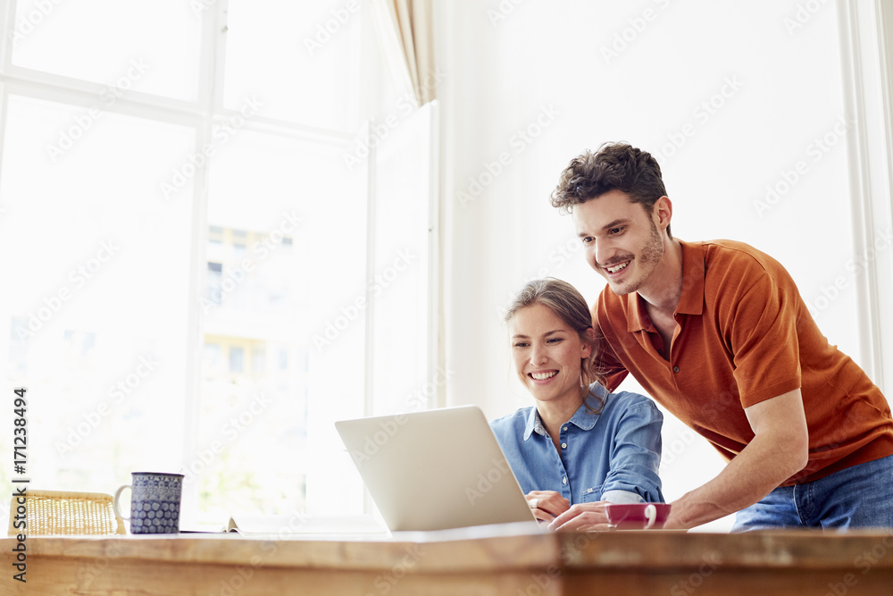 Smiling Young Couple Using Laptop At Table In House Smiling Young Couple Using Laptop At Table In House