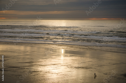 A distant woman walks her dog at sunset on the beach. Wet sand reflects the sky.