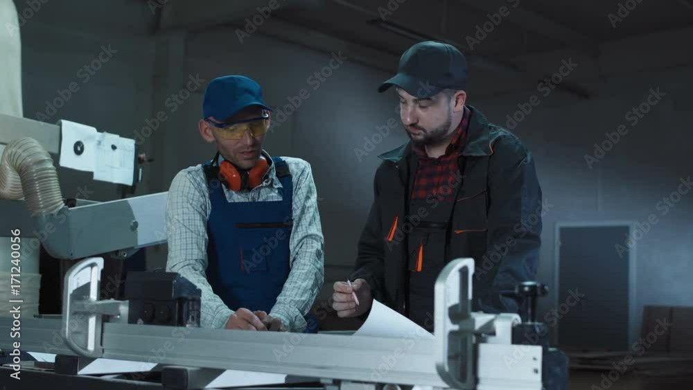 Carpenters standing in joinery shop and coworking with blueprints. Carpenters standing in joinery shop and coworking with blueprints.