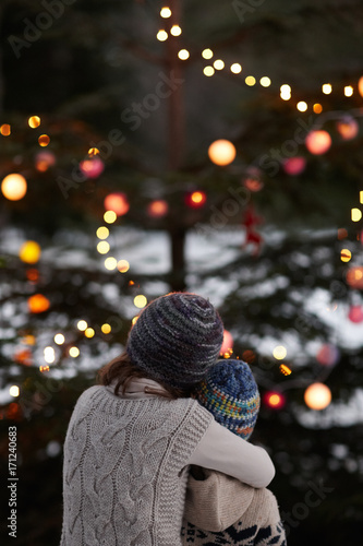 Two kids embraced in front of a lighted Christmas tree