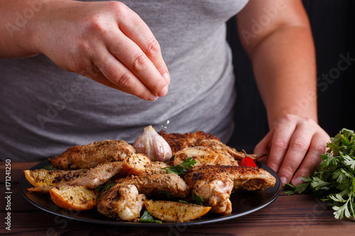 Woman adding salt to grilled chicken wings. Kitchen background,