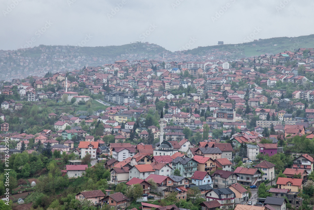 Aerial view of the hills of the suburbs of Sarajevo, Bosnia and Herzegovina during a cloudy and rainy day of spring. A mosque can be seen in front.