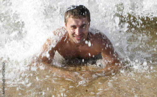 man on the shore lies. The sea wave covers the masculine. Beach vacation.