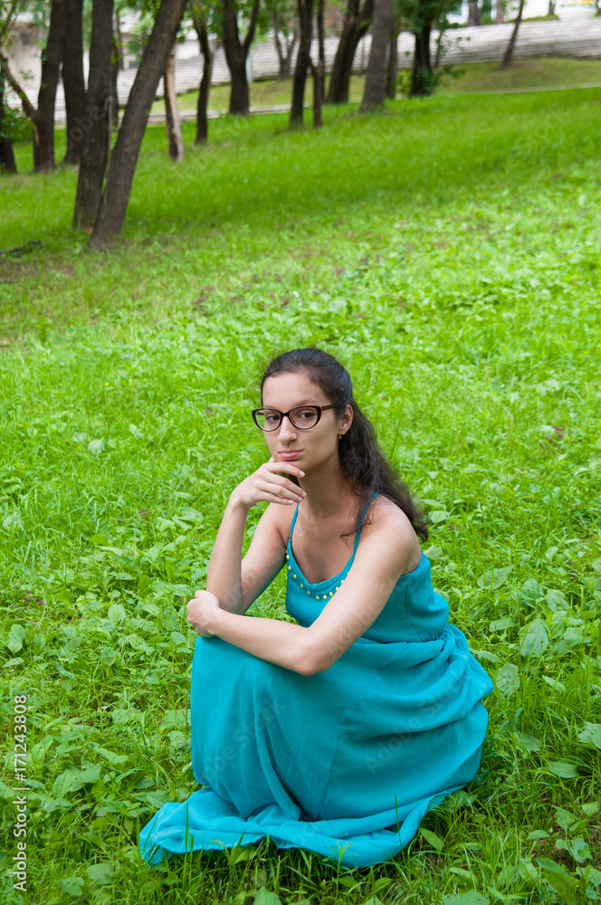 Girl in a green dress is sitting on lawn