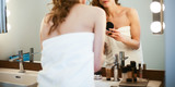 Young woman looking in the mirror and putting make-up on