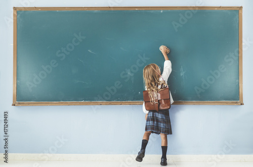 Rear view of little girl cleaning blackboard in classroom photo