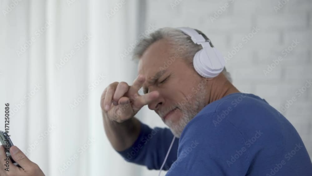 Male retiree in headphones enjoying favorite song from cellphone and dancing Male retiree in headphones enjoying favorite song from cellphone and dancing