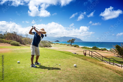 Golfer with straw hat teeing off with driver from ocean side par 4 hole photo