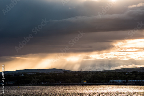 Landscape view of Ile D'Orleans, Quebec, Canada during sunset with sun rays, large stormy clouds and Saint Lawrence river