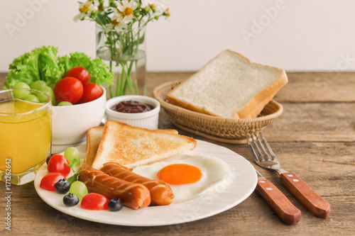 Homemade breakfast with sunny side up fried egg toast sausage fruits vegetable strawberry jam and orange juice in side view with copy space.Delicious homemade american breakfast concept for background