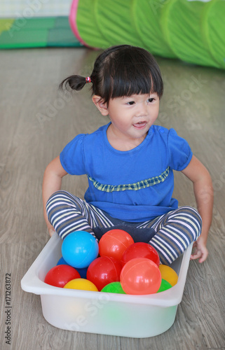 Asian Child playing colorful balls in plastic tray at the kid room.