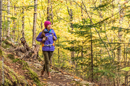 Autumn hike backpacker lifestyle woman walking on trek trail in forest outdoors with yellow leaves foliage. Fall outdoor activity. Asian girl hiking outside with backpack and cold season camping gear. © Maridav