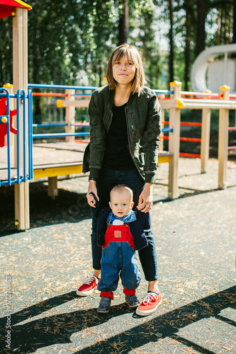 Young mother with her beautiful son stands at the playground. Outdoors healthy child activity, active lifestyle and having fun on family summer vacation with son at the playground