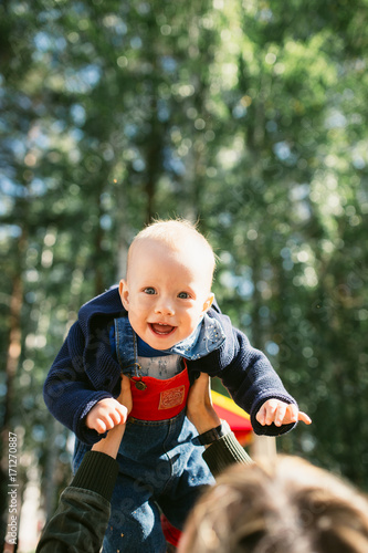 Mother hands tossing up the high air joyful baby boy. Outdoors healthy child activity, active lifestyle and having fun on family summer vacation with son at the playground.